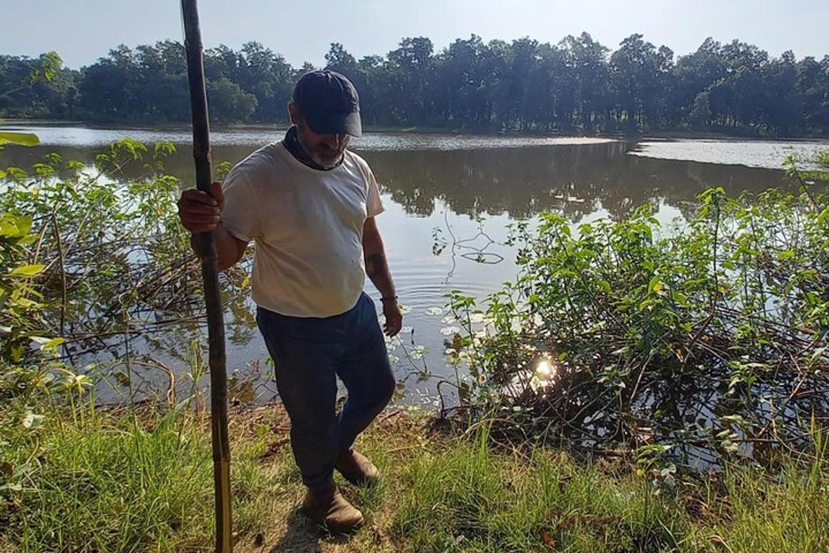 seorang lelaki memegang tiang di hadapan sebuah tasik