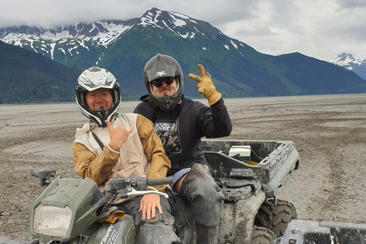 Tveir menn sitja á fjórhjóli með fjöll í bakgrunni