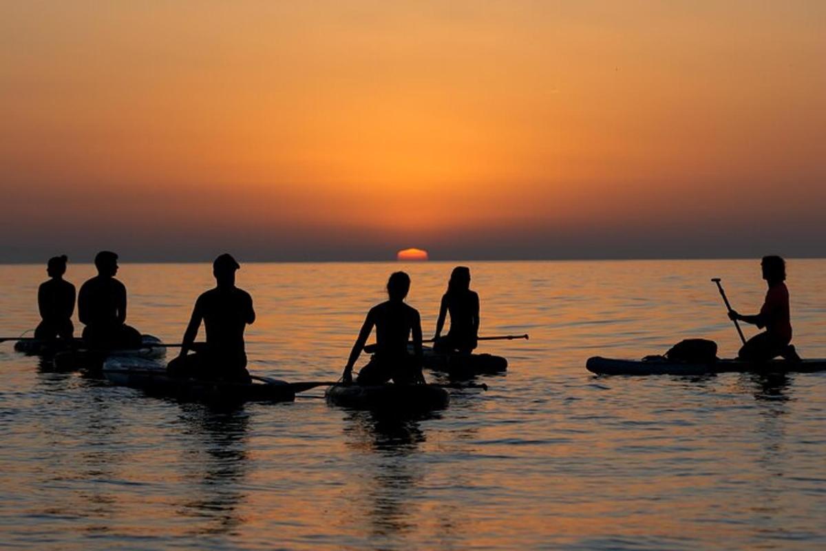 um grupo de pessoas sentadas em caiaques na água ao pôr do sol