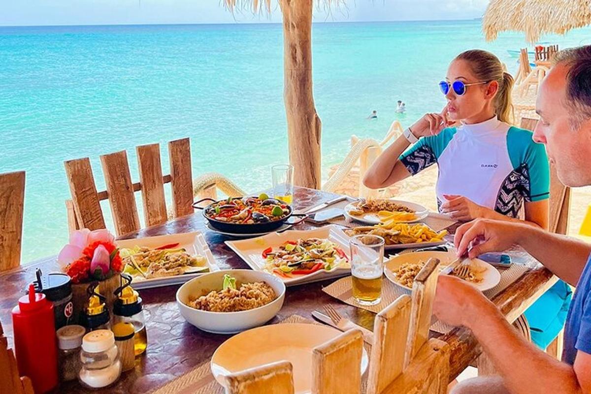 a group of people sitting at a table with food on the beach
