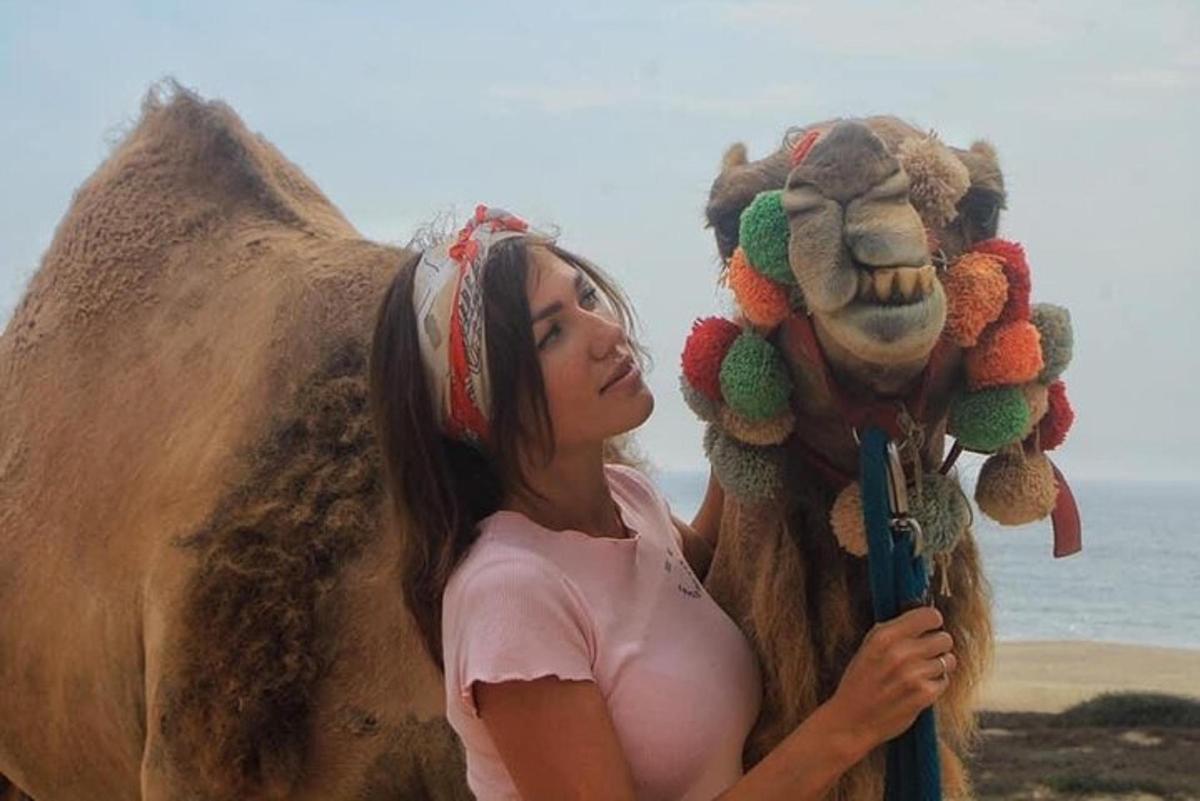 een vrouw die een opgezette kameel vasthoudt op het strand