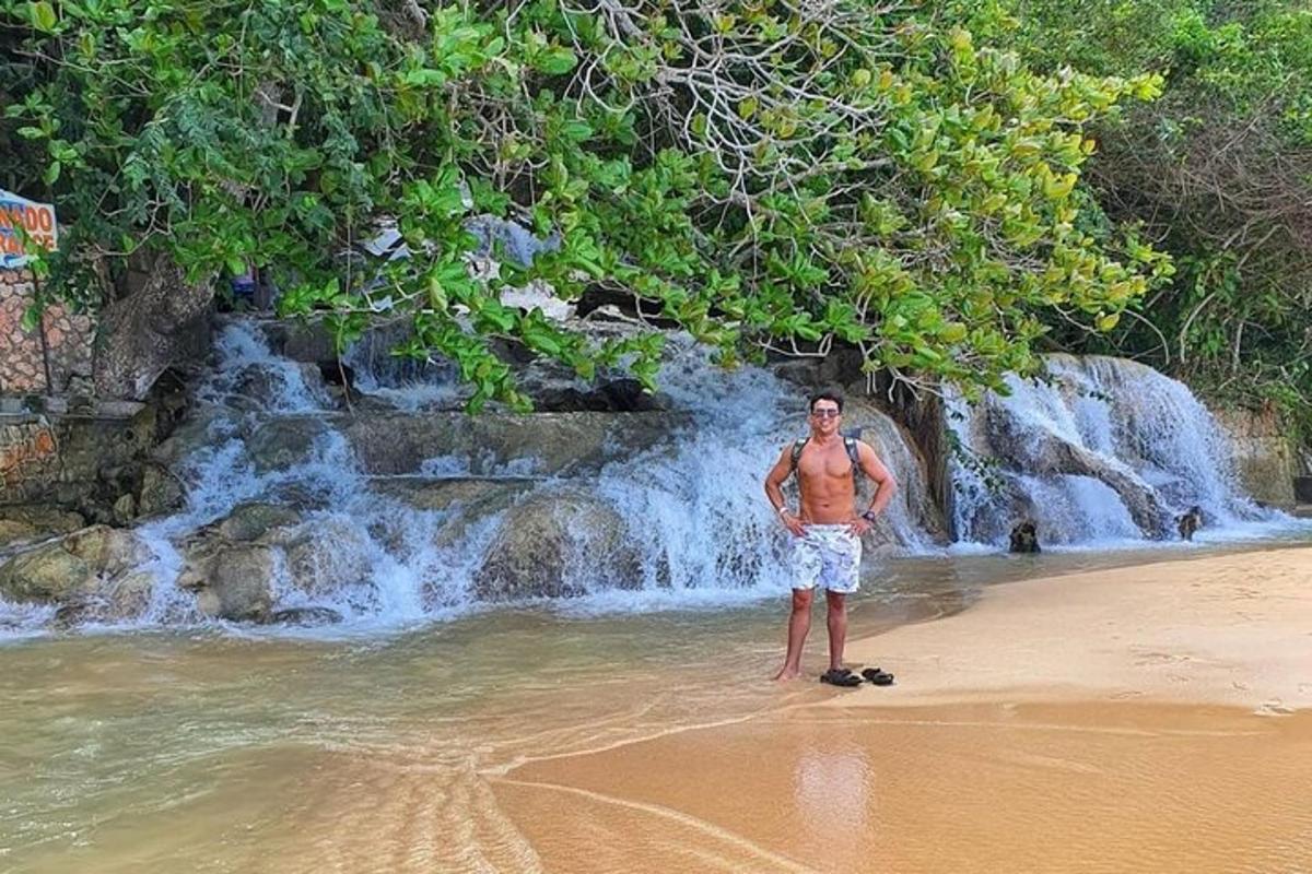 Un hombre parado en la playa frente a una cascada
