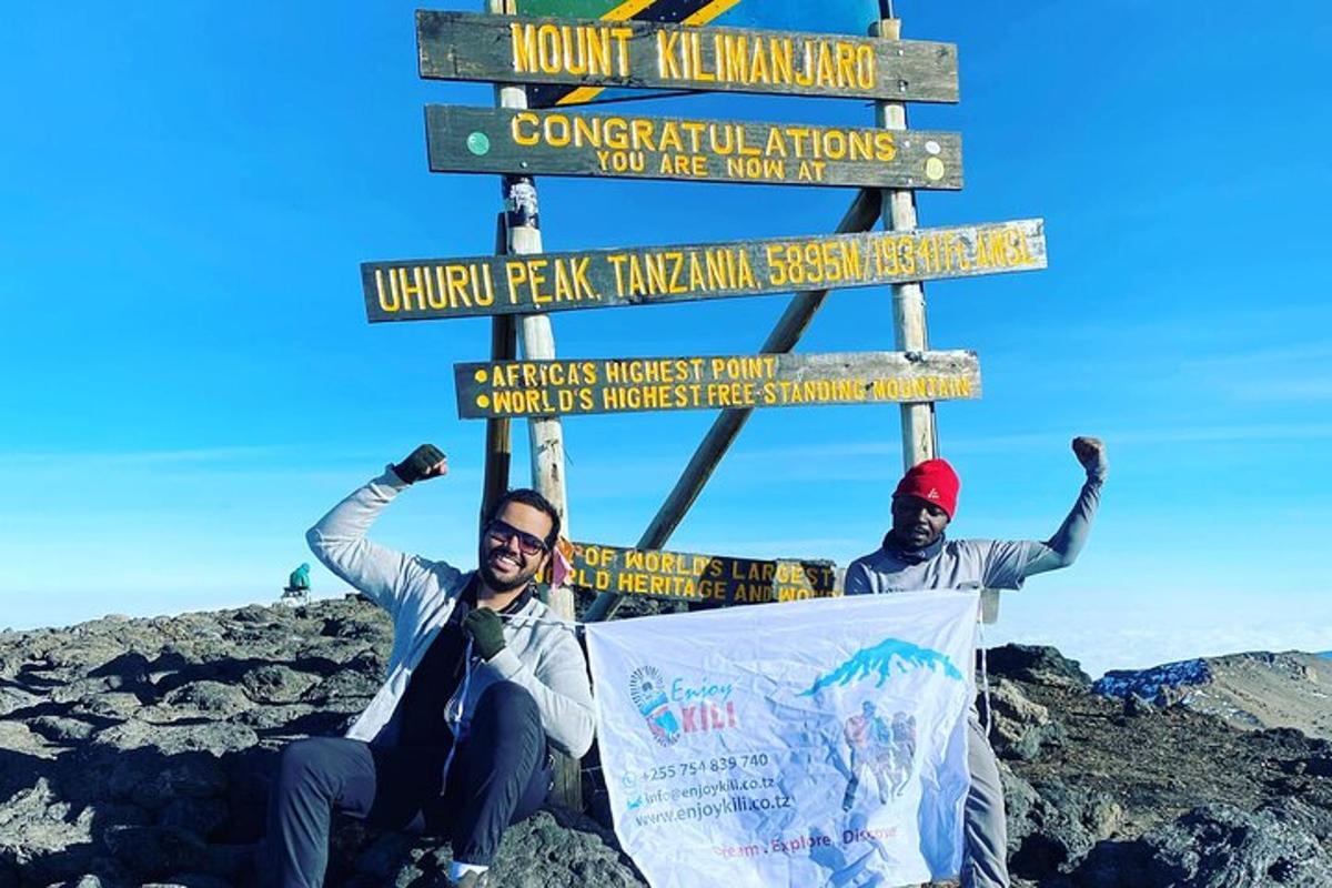 dua lelaki sedang bergambar di hadapan papan tanda di atas gunung