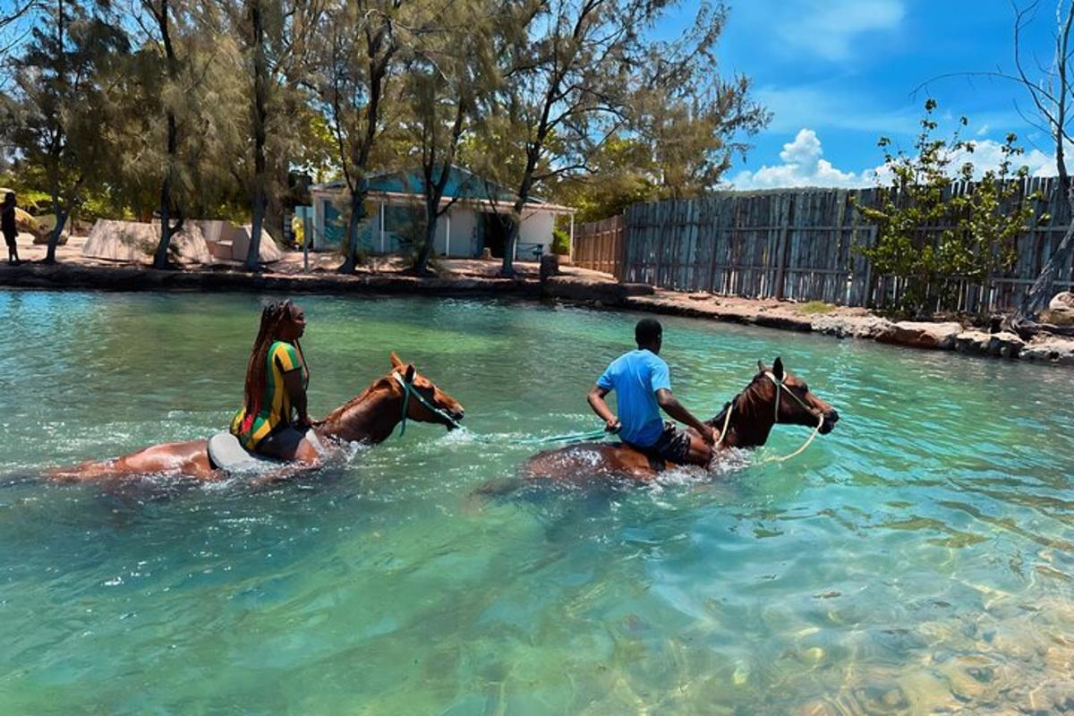 zwei Personen reiten auf Pferden in einem Gewässer