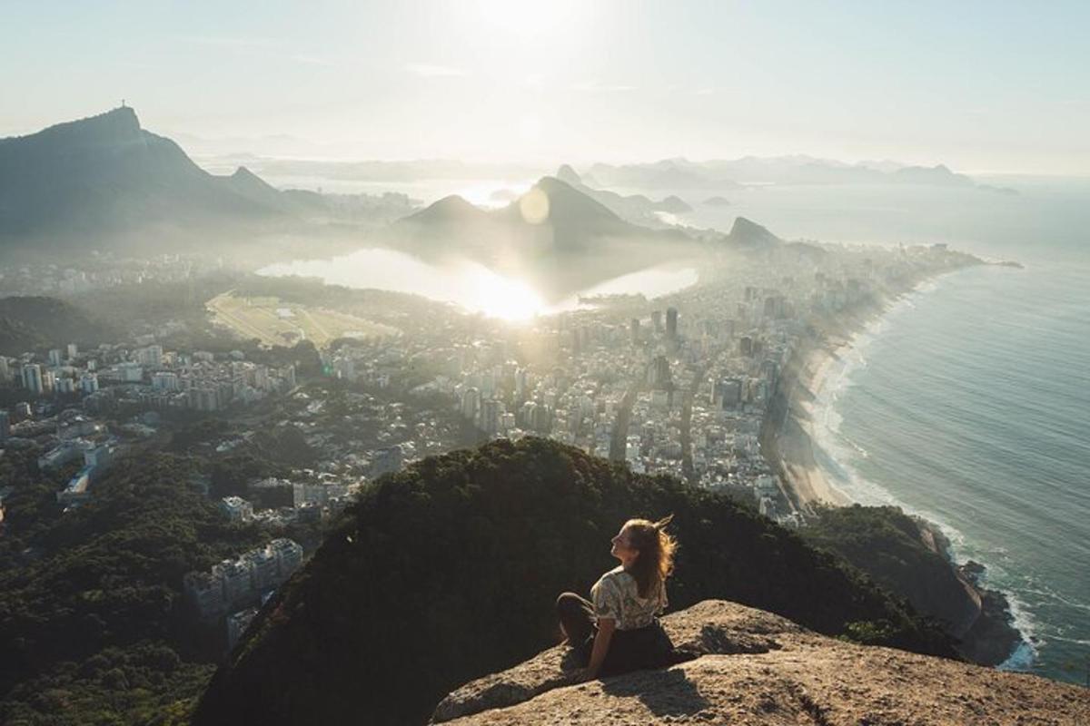 uma mulher sentada no topo de uma montanha com vista para uma cidade