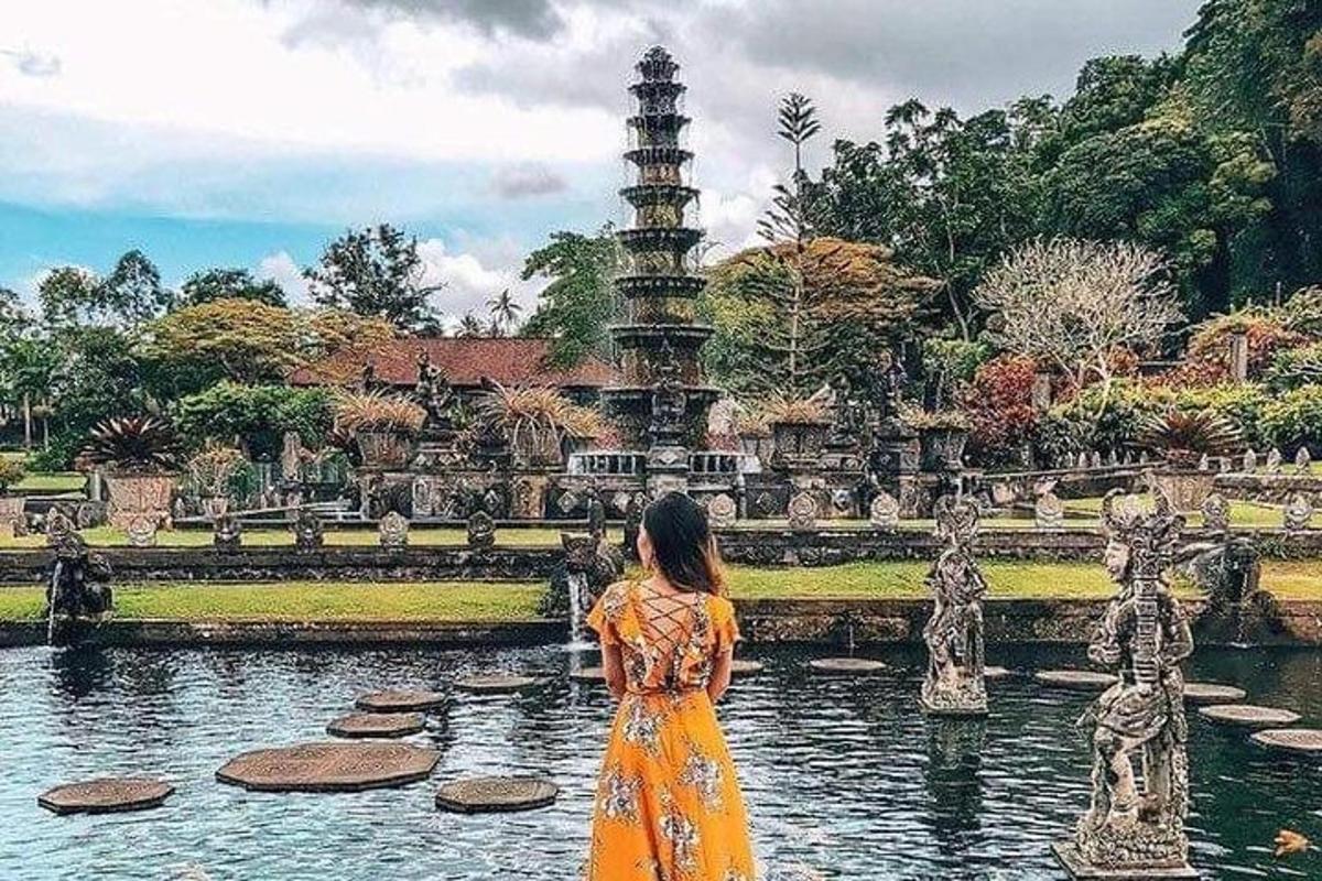 seorang wanita berpakaian oren berdiri di hadapan air pancut