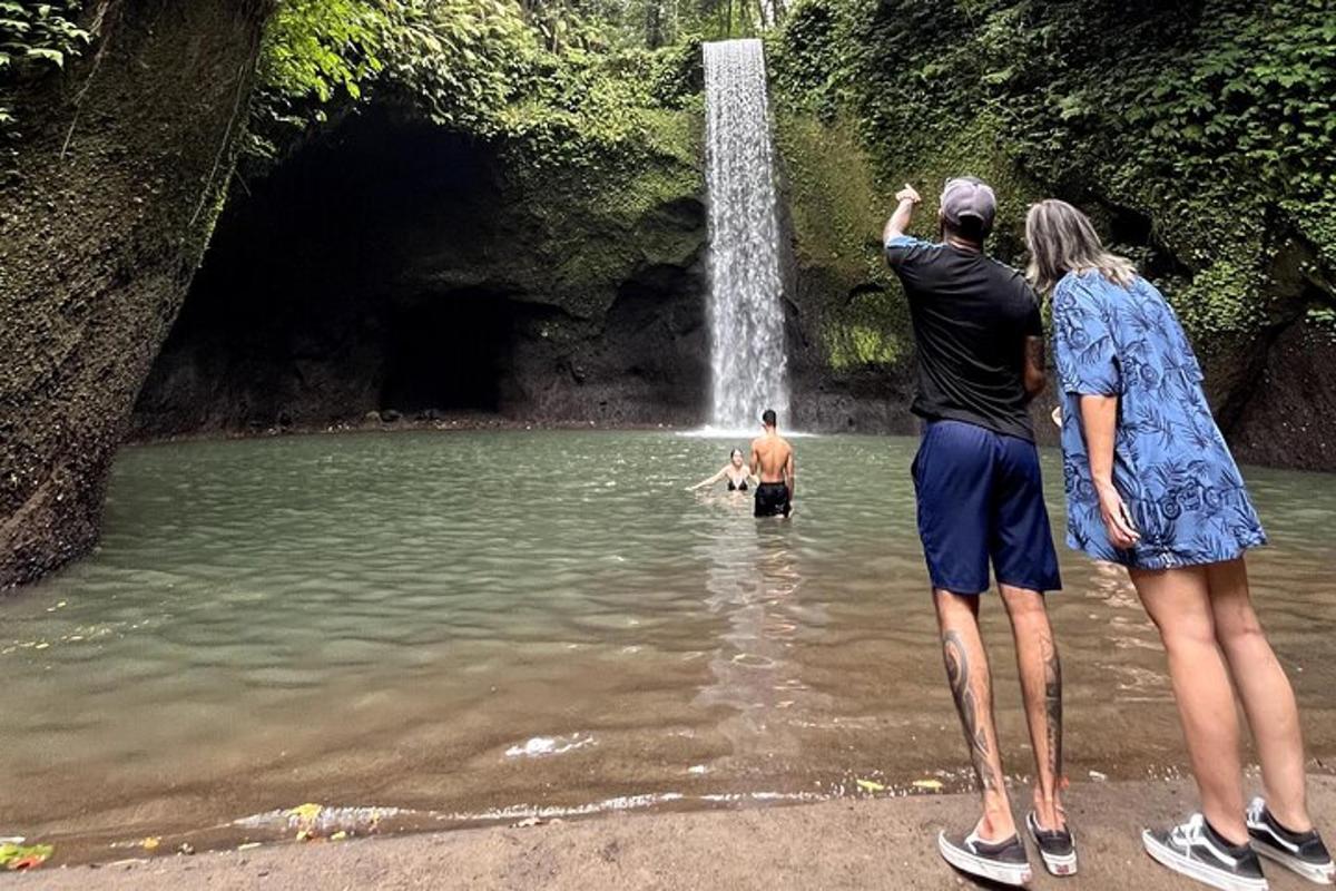 two people standing in the water near a waterfall