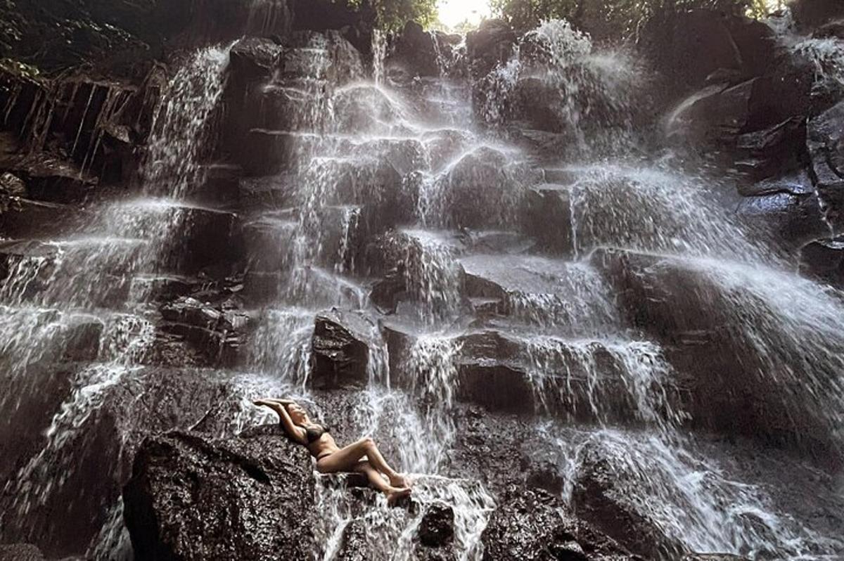 a woman laying on a rock in front of a waterfall