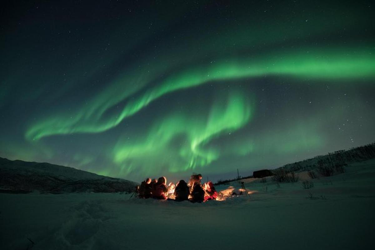 isang grupo ng mga tao na nakaupo sa paligid ng apoy sa ilalim ng aurora