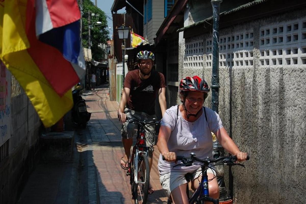 Dos personas andando en bicicleta por una calle con una bandera