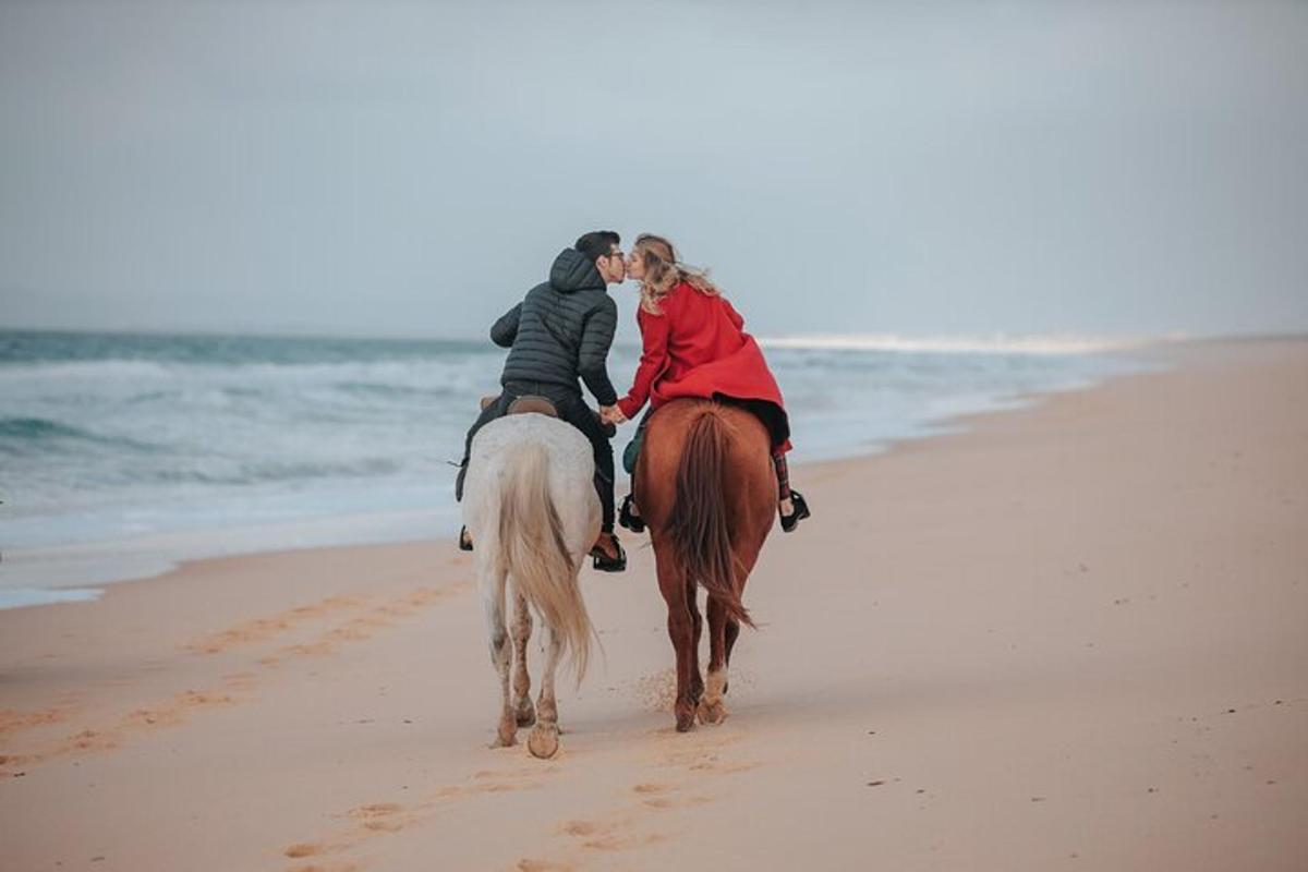 dues persones muntant a cavall a la platja