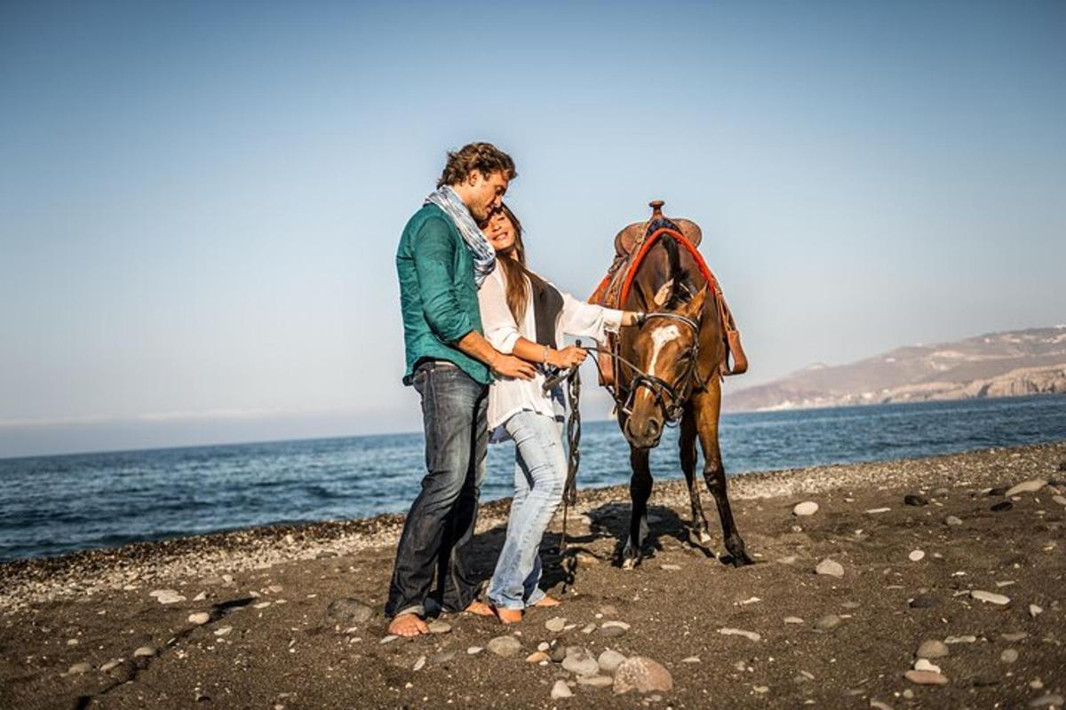 un uomo e una donna in piedi accanto a un cavallo sulla spiaggia