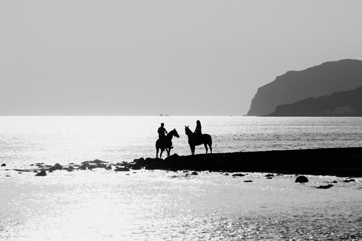 two people riding horses on the beach near the water