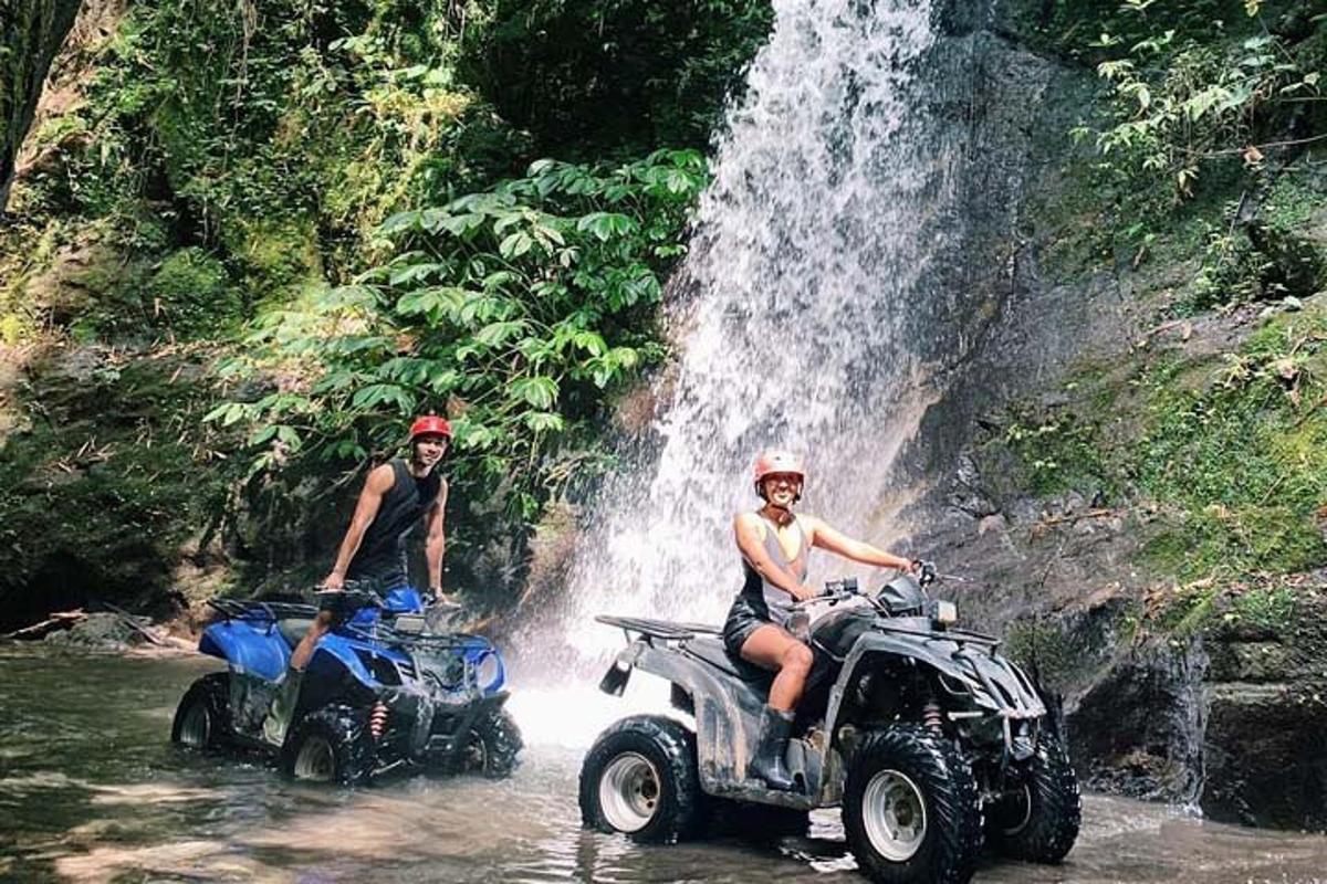 Două persoane pe ATV-uri în apă lângă o cascadă