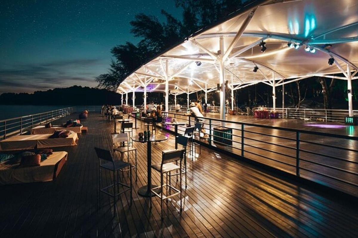 a deck with tables and chairs on the water at night