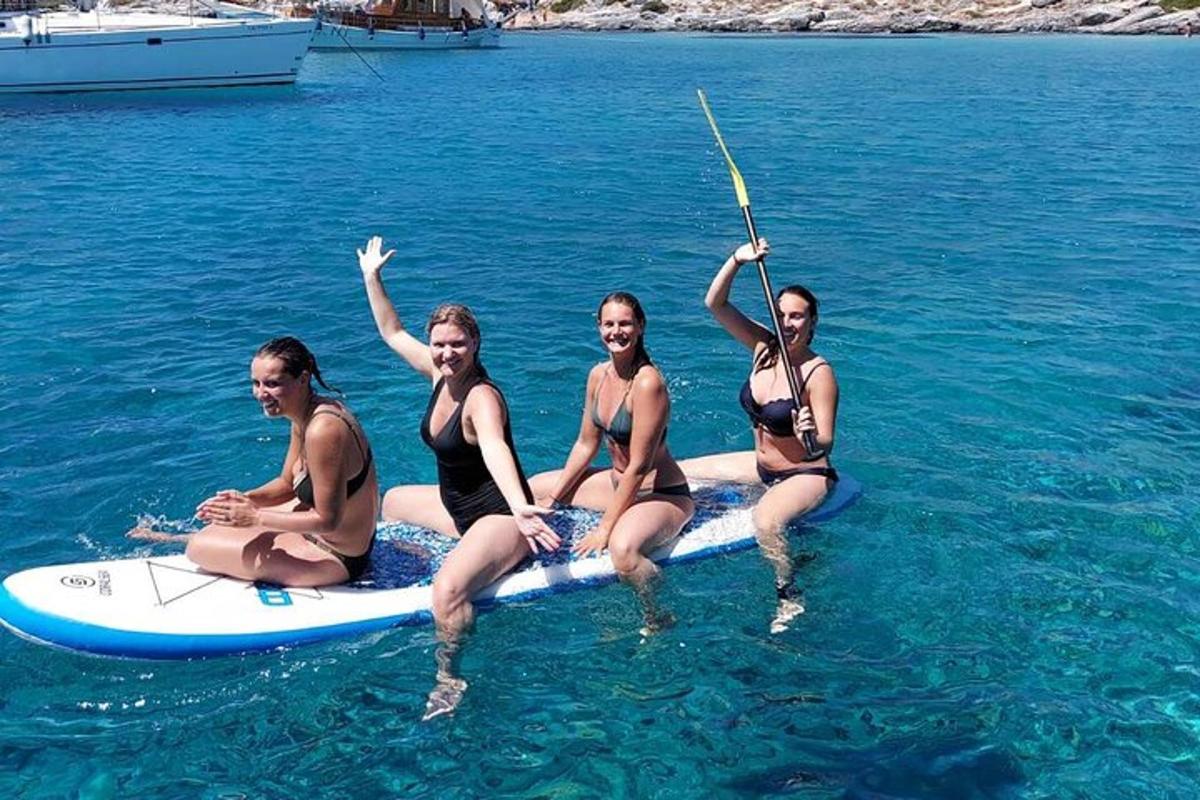 четири жене у купаћим костимима седе на дасци за сурфовање у води