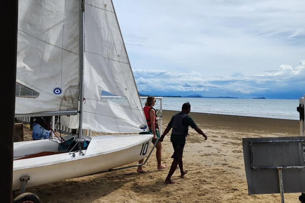 un uomo e una donna che camminano sulla spiaggia con una barca a vela