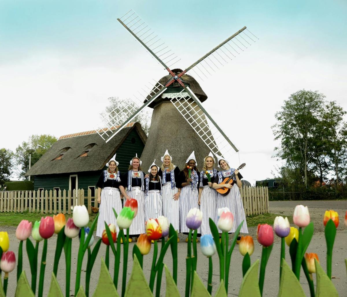 Un grupo de chicas de pie frente a un molino de viento.