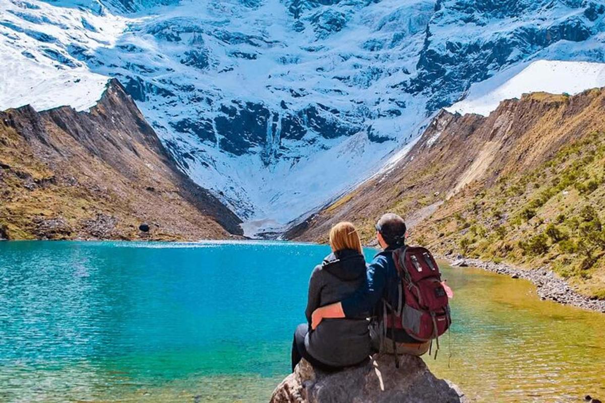 pasangan yang duduk di atas batu yang menghadap ke tasik gunung