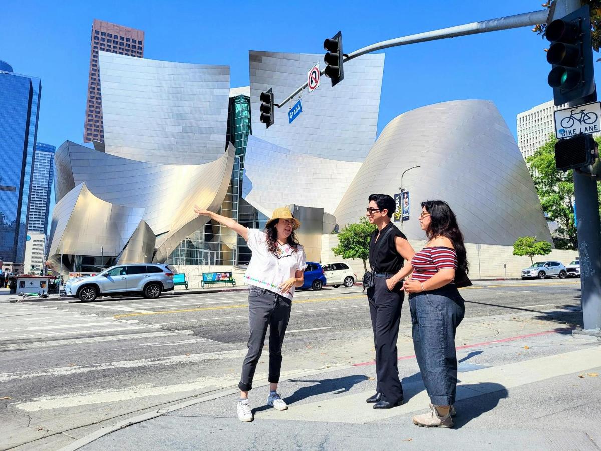 three people waiting to cross a street at a traffic light