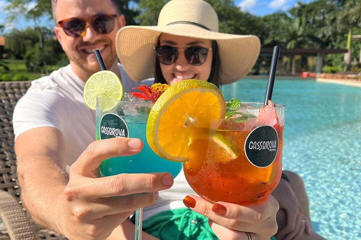 a man and a woman holding two cocktails by a pool