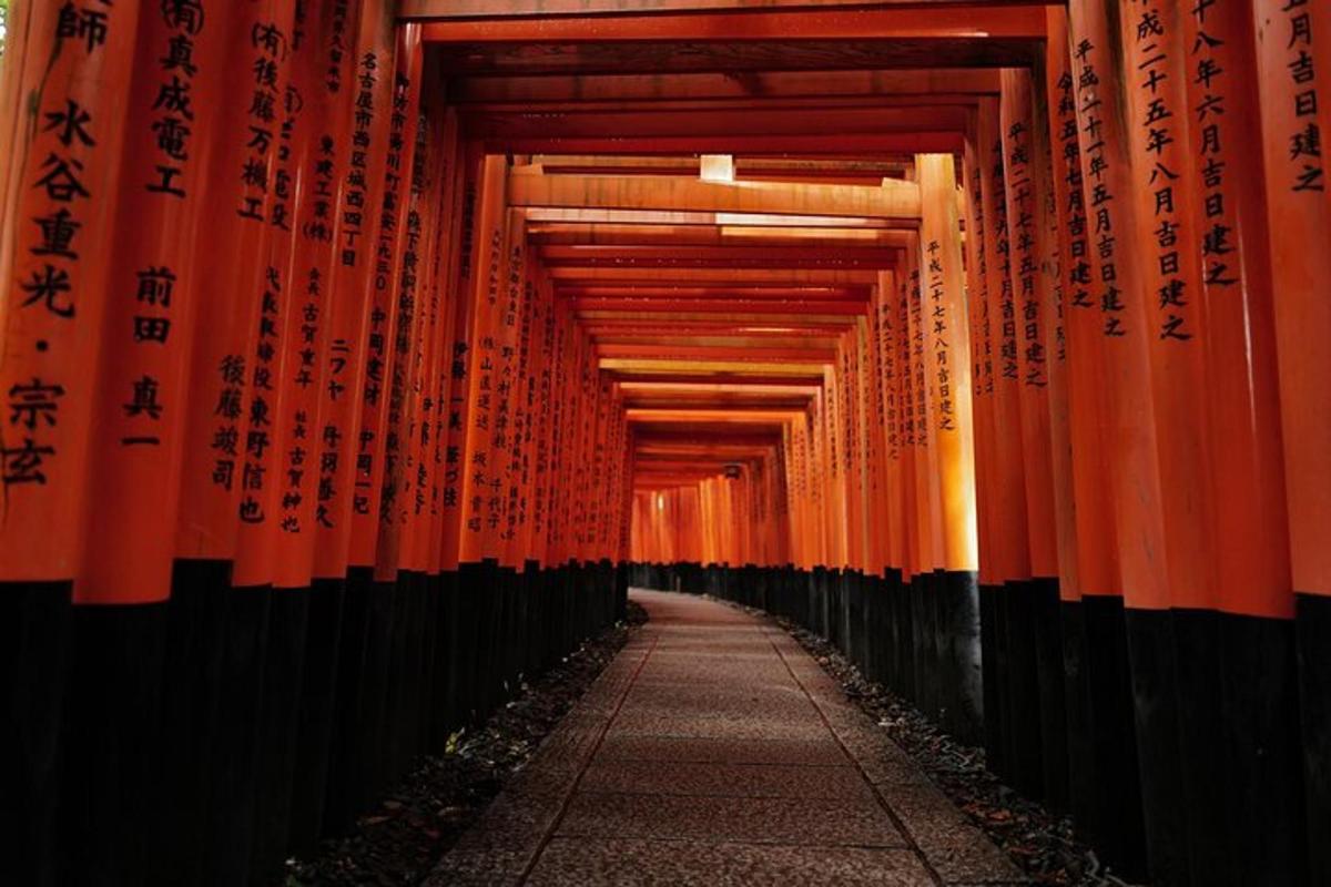 Un pasillo de puertas torii naranjas con escritura en ellas.