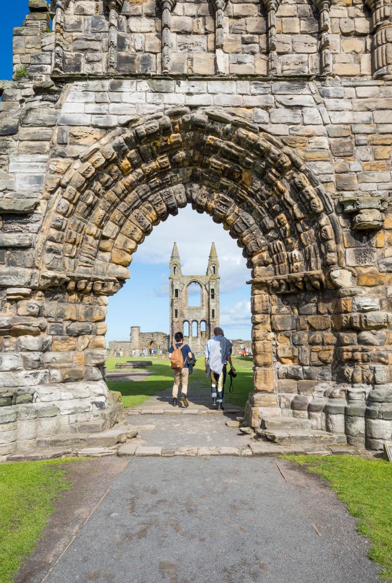 two people walking through a stone archway with a church in the background