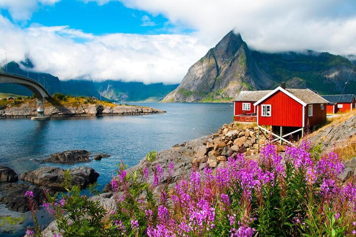a red house on the side of a lake with mountains