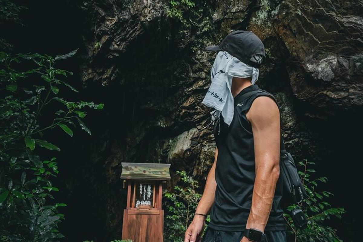 a man with a bandana on his face standing in front of a rock