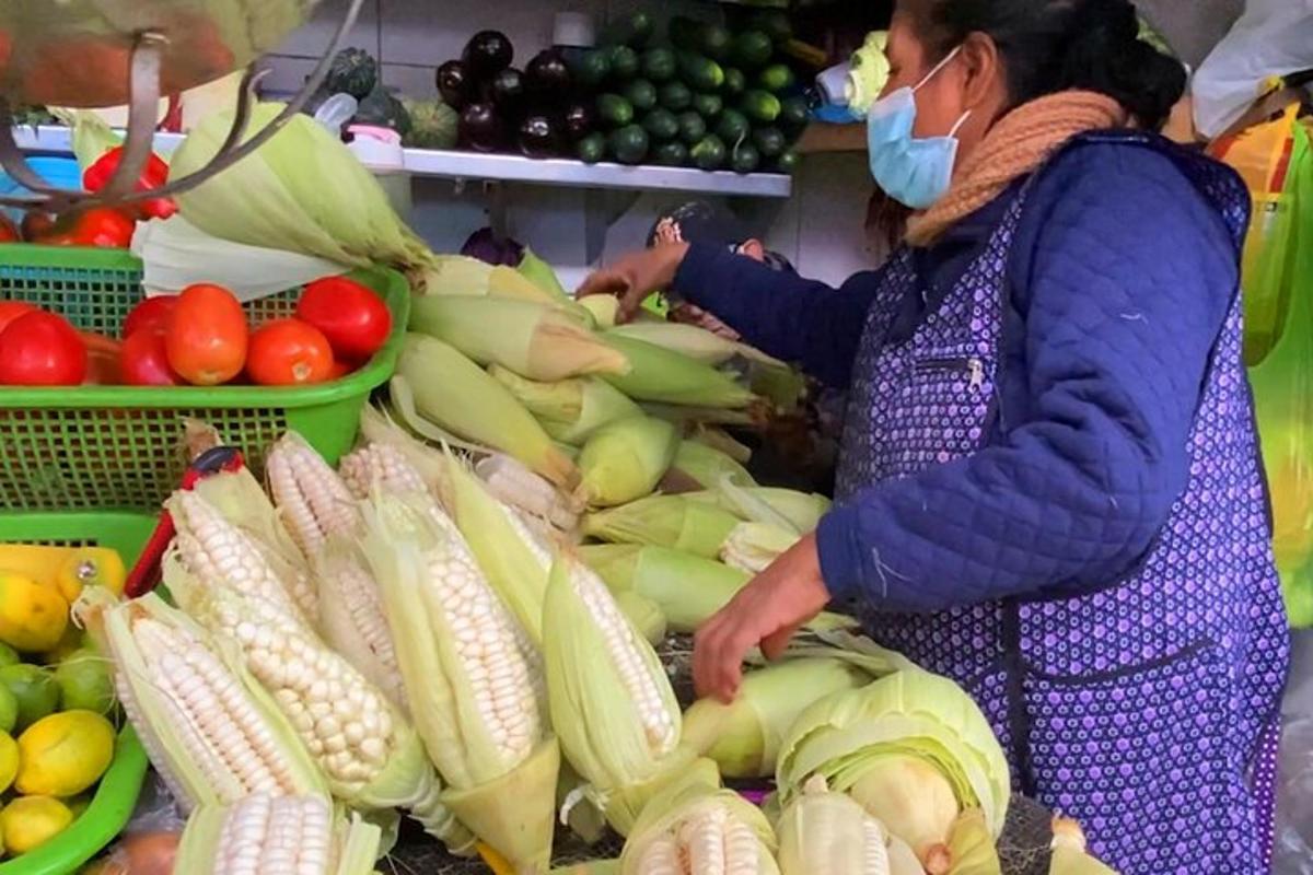 seorang wanita memakai topeng muka berdiri di pasar dengan sayur-sayuran