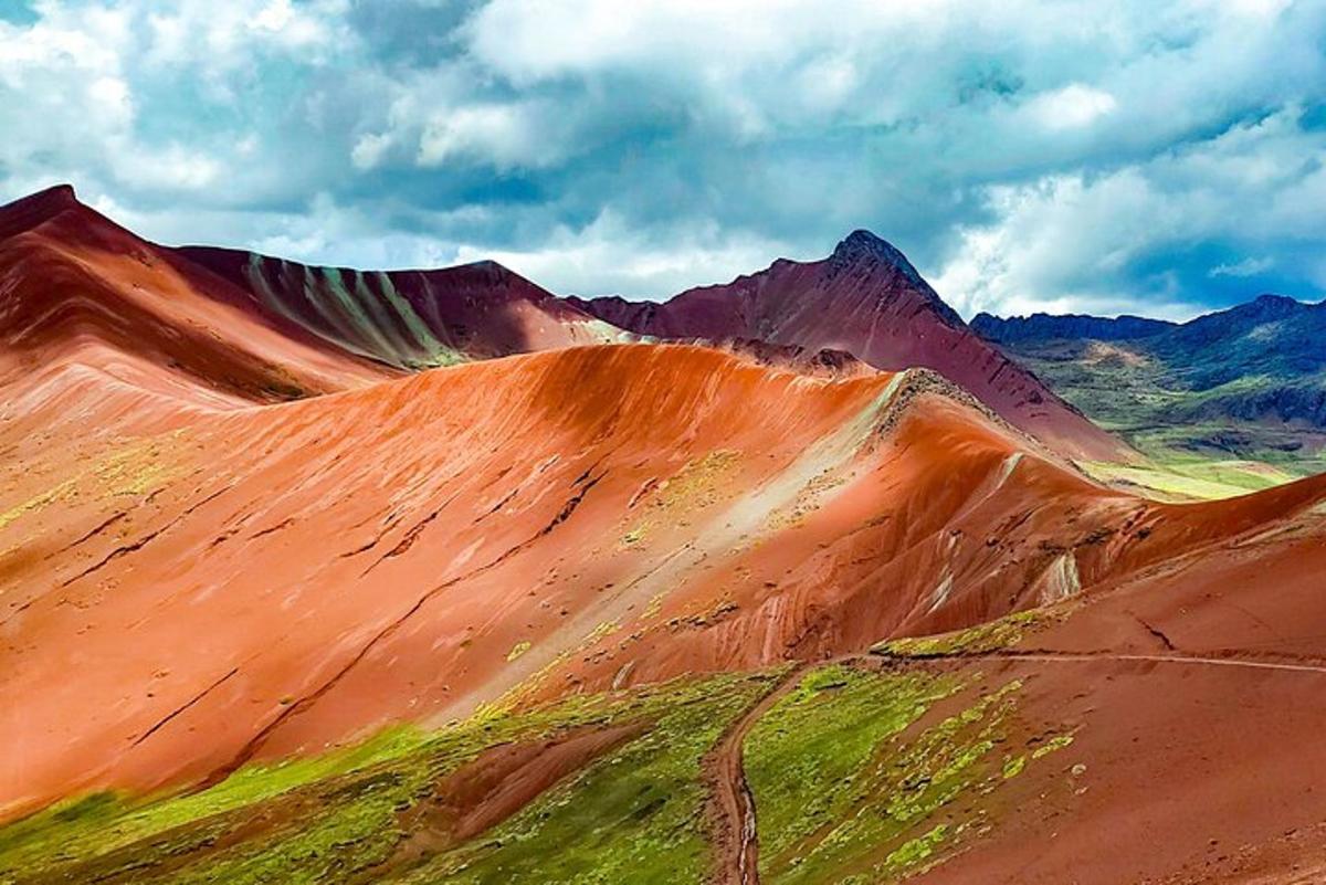 una collina sterrata con erba e montagne sullo sfondo