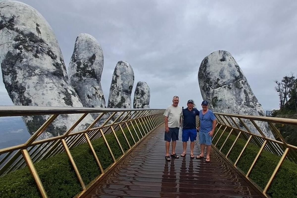 um grupo de três pessoas em pé em uma ponte em frente a uma estátua