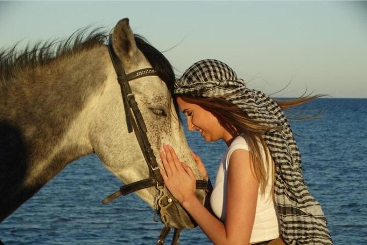 Una mujer está de pie junto a un caballo.