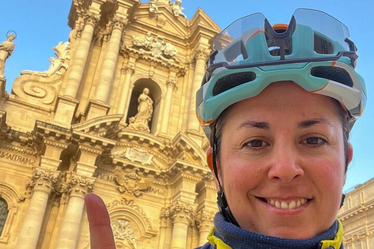 Una mujer que lleva un casco y hace un gesto de aprobación con el pulgar frente a un edificio.