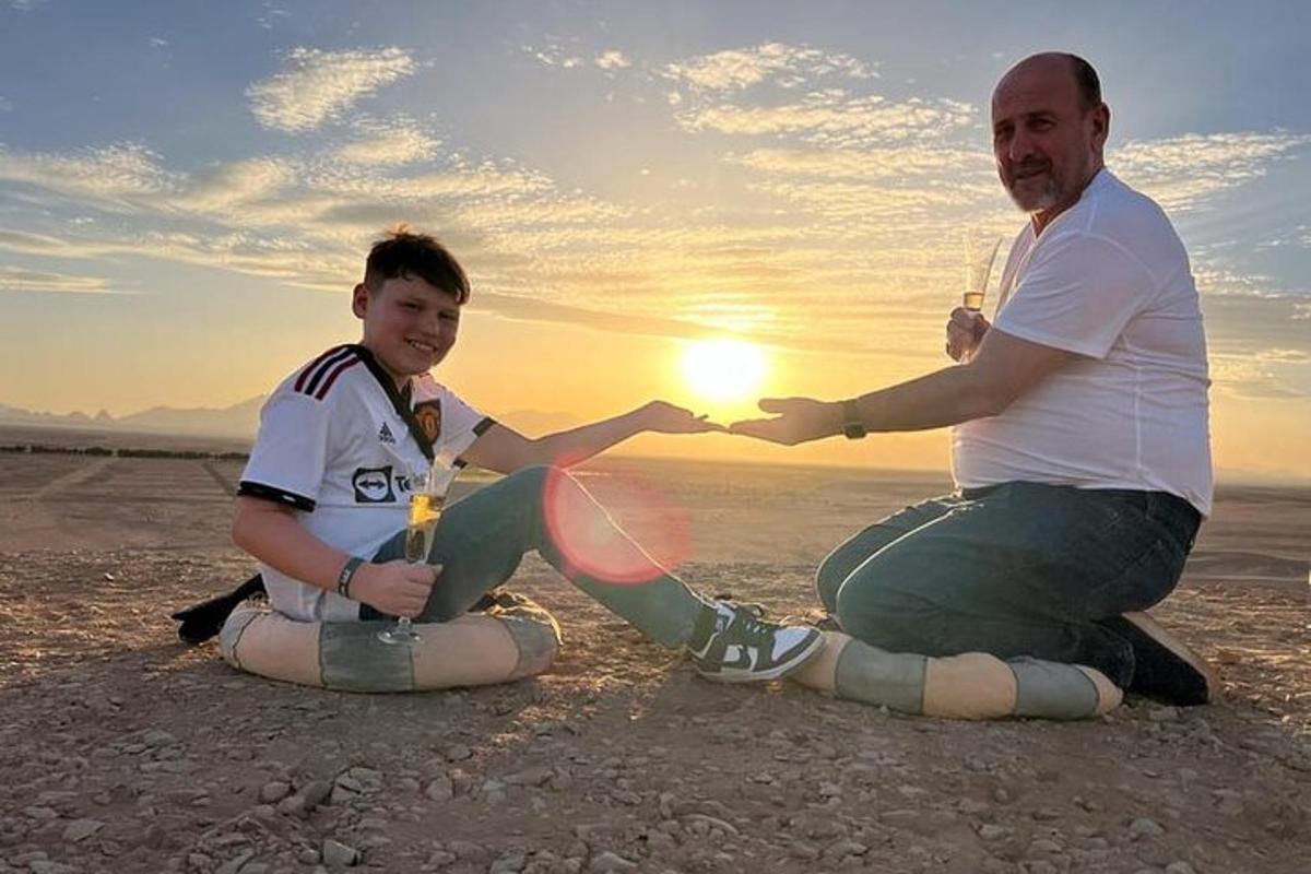 Човек и дечак седе на плажи у залазак сунца