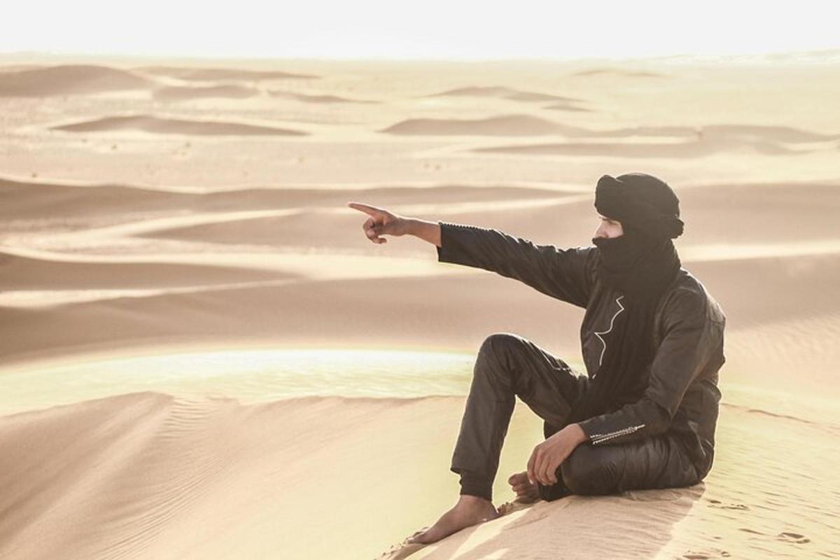um homem sentado em uma duna de areia no deserto