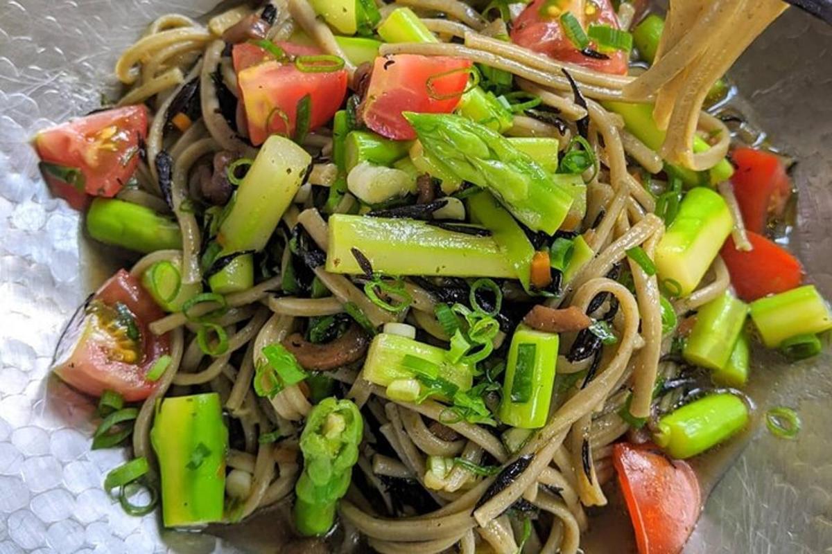 a bowl of noodles and vegetables with a wooden spoon