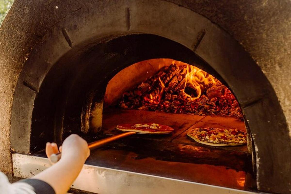 Egy személy pizzákat tesz egy téglaégető kemencébe