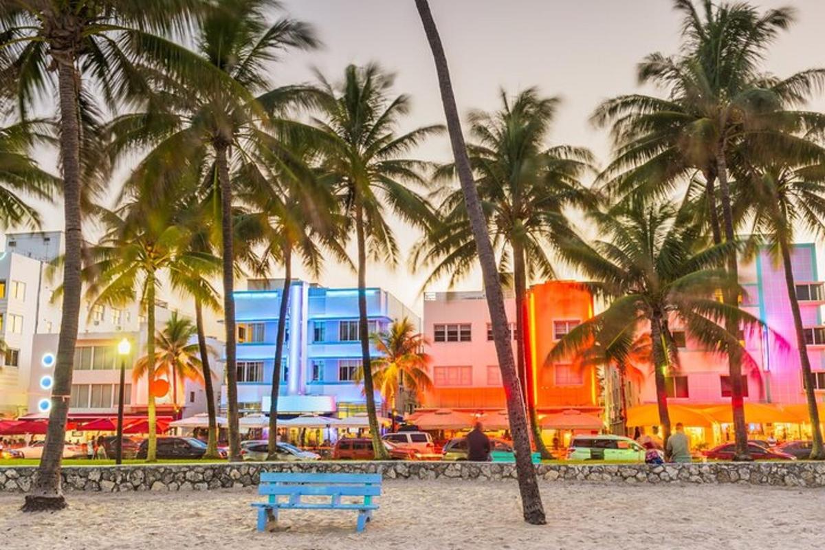 Un banco azul en una playa con palmeras y edificios.