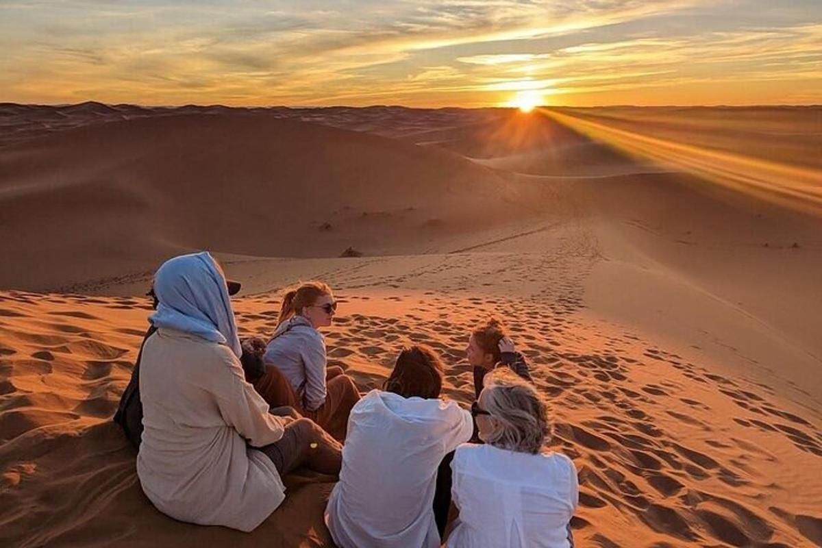 a group of people sitting in the desert watching the sunset
