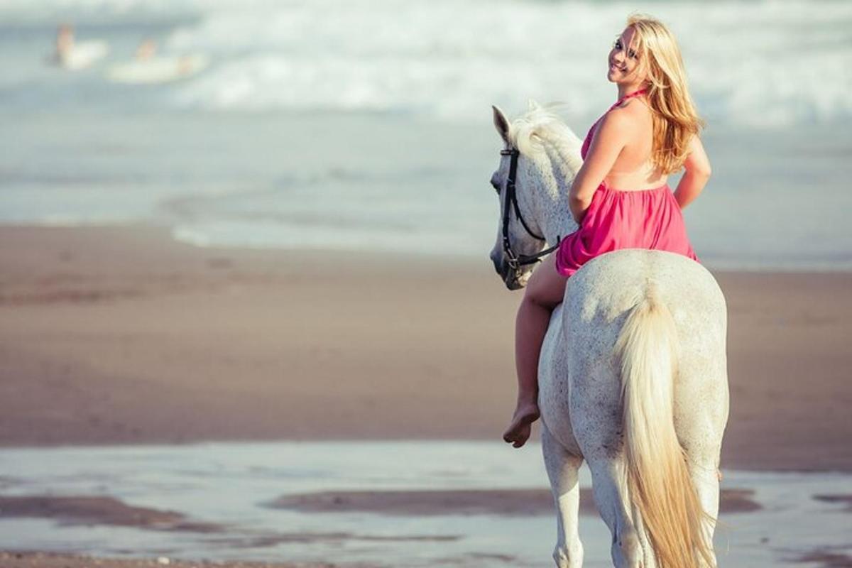 eine Frau in einem roten Kleid, die auf einem weißen Pferd am Strand reitet