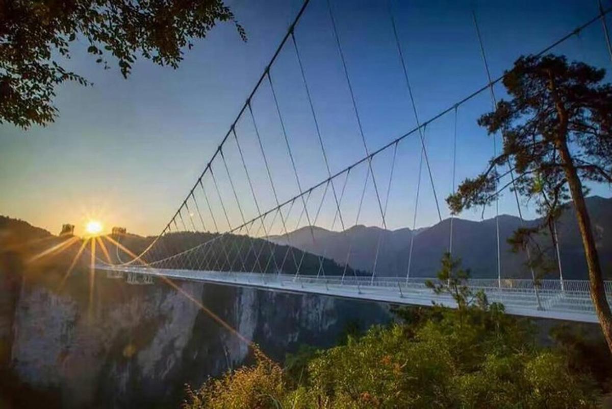 a suspension bridge over a lake with the sun setting