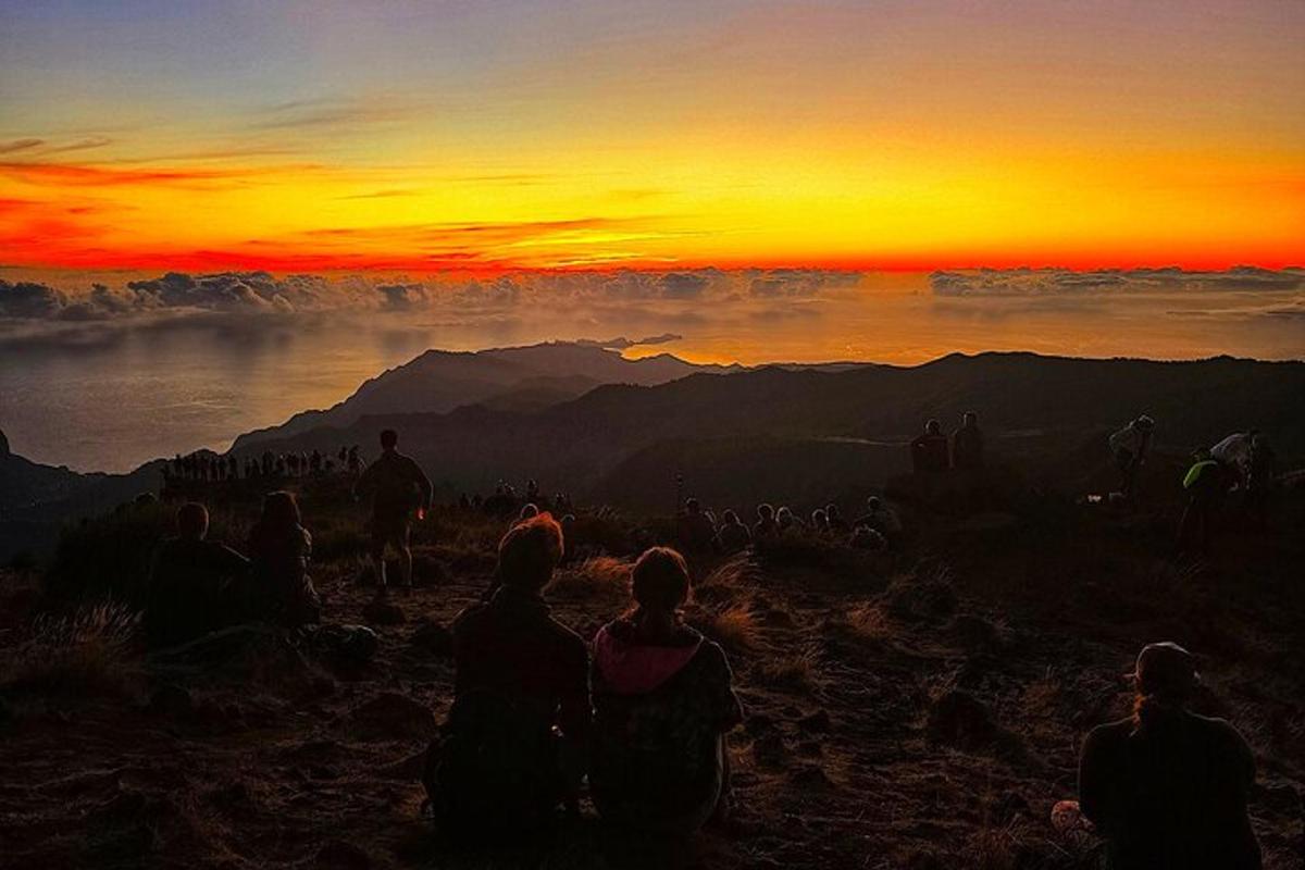 un gruppo di persone sedute su una montagna a guardare il tramonto