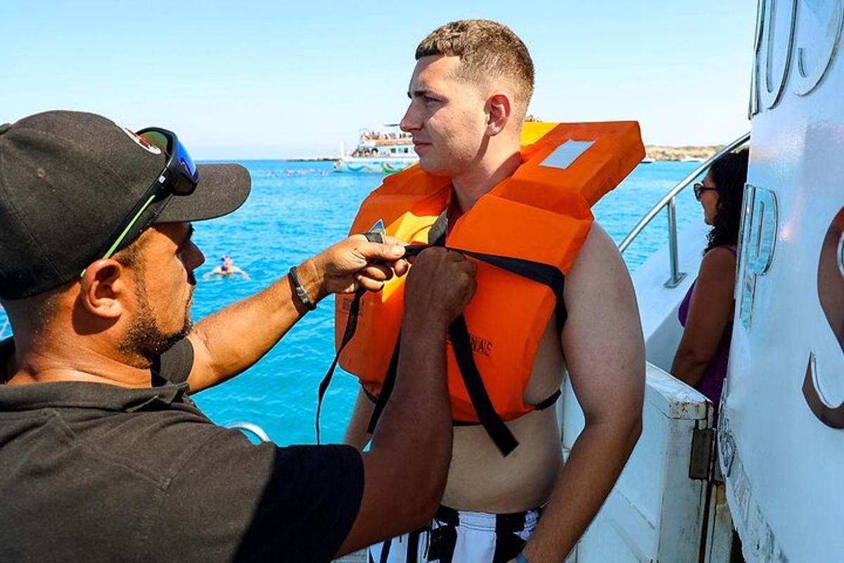 moški v oranžnem rešilnem jopiču, ki mu pomaga moški na čolnu