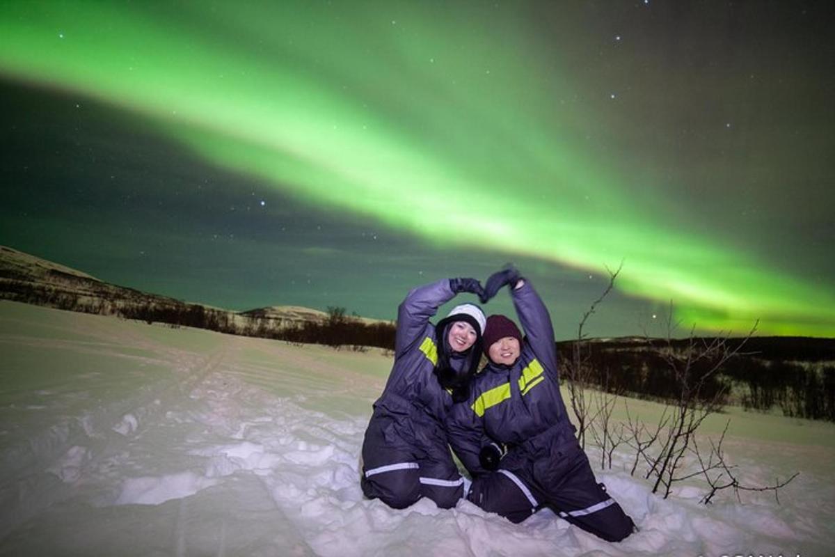 due persone sedute nella neve sotto l'aurora