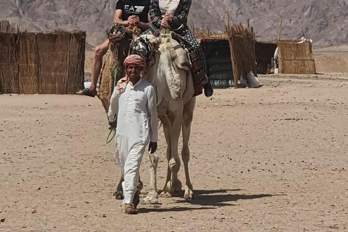 a man walking a camel with two people on it