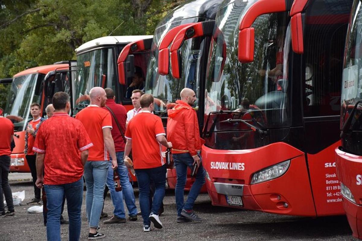 um grupo de homens de camisas vermelhas parados em frente a ônibus