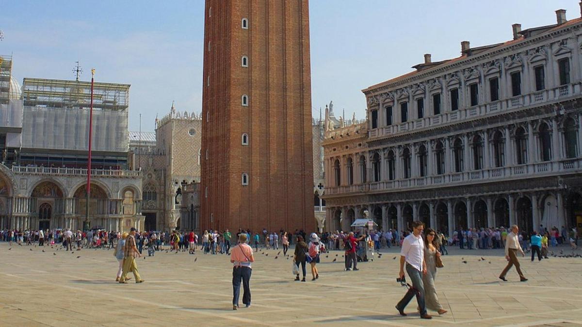 a group of people walking in a square with a clock tower