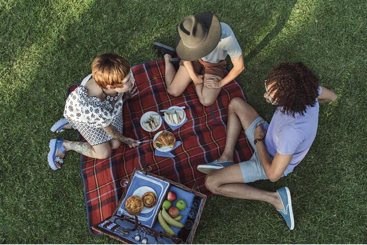drei Personen sitzen auf einer Picknickdecke mit einem Teller Essen