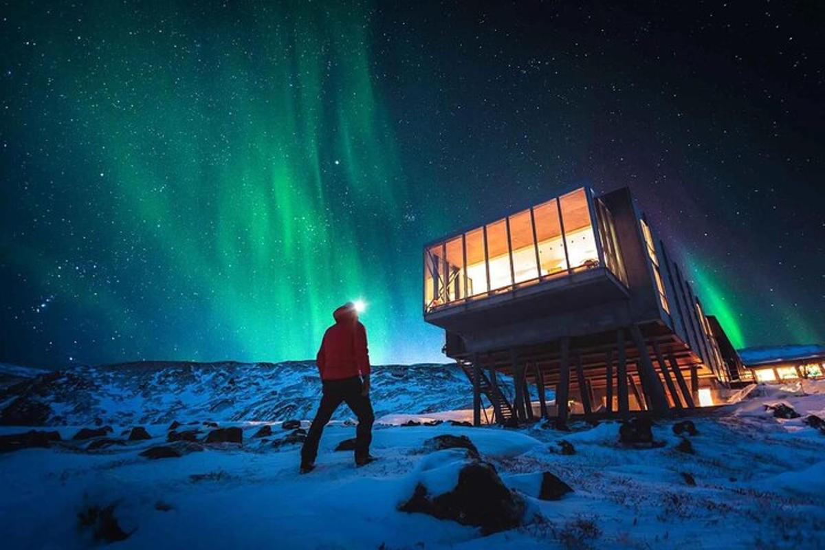 muž stojící ve sněhu před observatoří s polární září